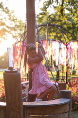 Adorable child in pink dress playing on the playground holding the rope