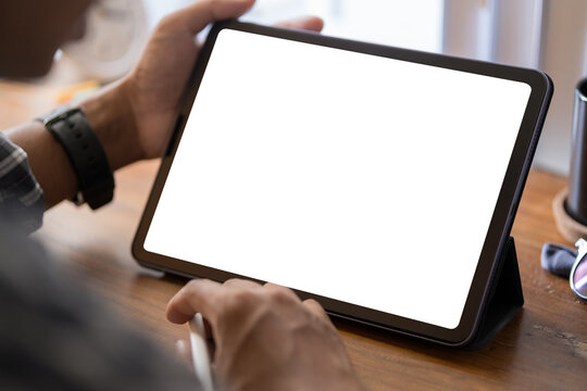 Over Shoulder View Of Young Man Using Digital Tablet On White Table At Home Office.