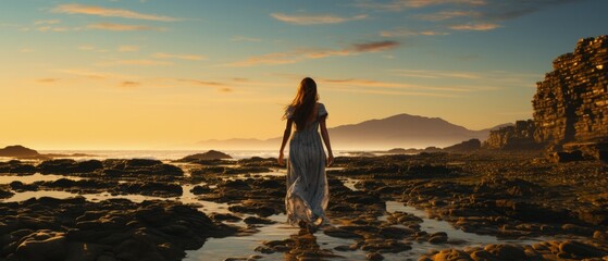 Back view of a woman in flowing dress walking along a rocky shoreline during sunset with vast sea behind.

 - Powered by Adobe