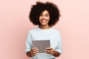 Fictional young black woman holding a tablet and smiling. Isolated on a plain pink background....