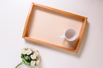 Bandeja de madera con taza de café vacía y ramo de flores sobre la mesa. Maqueta como recurso...
