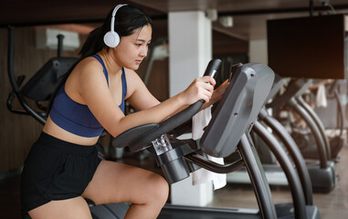 Fototapeta na wymiar Young woman in sportswear, burning calories, cycling bikes in gym.