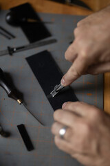 Man doing leatherwork, in a leather working workshop, making a black leather belt