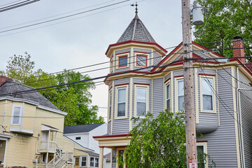 Fancy blue house with partial tower with bay windows and red trim with wind vine on roof
