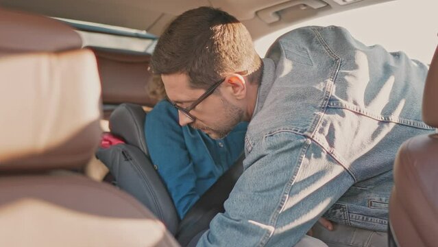 Male firmly fastens two children with seat belts. Joyful family preparing for car trip. Priority to safety while traveling on road. Safe transportation of children. Family travels.