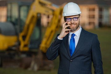 Construction builder manager or supervisor at a construction site. Portrait of construction manager worker in hardhat and suit near excavator. Renovation with construction manager or supervisor.