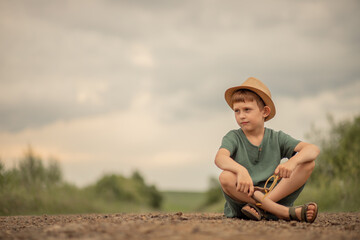 Naklejka na ściany i meble child boy in a hat with a slingshot in his hands sits on the road