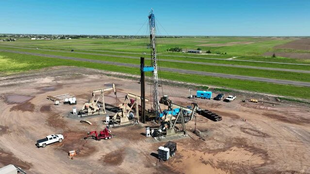Wide orbit around oil drilling operation with oil derricks and oil rig for fracking. Aerial establishing shot of rural USA oil facility.