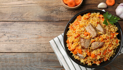 Delicious pilaf with meat, carrot and garlic on wooden table, top view. Space for text