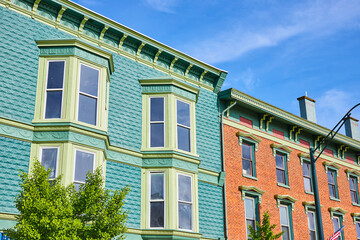 Fototapeta na wymiar Bay windows on teal brick building with tops of green trees and adjoined to a red brick building