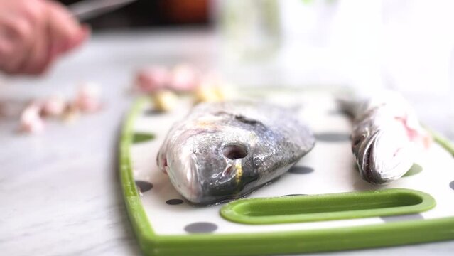 hand peeling garlic next to a sea bream and a whiting on the work surface