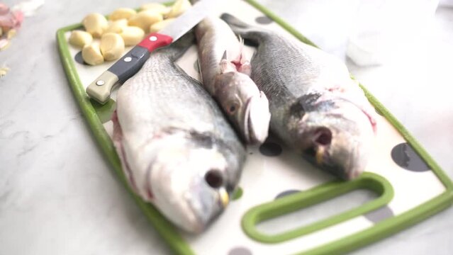 hand peeling garlic next to a sea bream and a whiting on the work surface