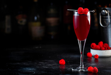 Raspberry Rossini alcoholic cocktail drink with prosecco, cava, or sparkling wine with raspberry puree and ice, dark bar counter background, copy space