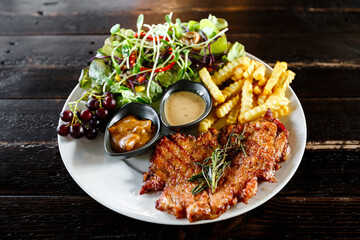 Grilled beef or pork steak with fried potato, vegetables and herbs salad on wooden table