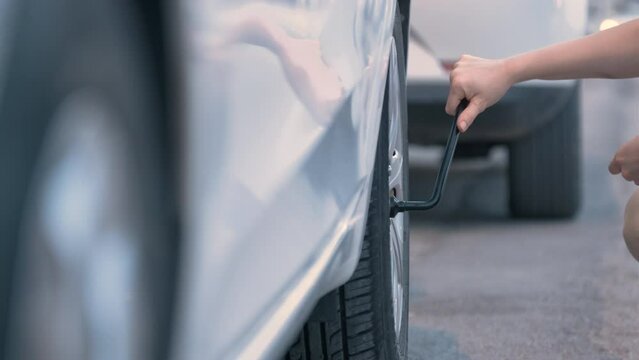 The Woman Try to Check Tire, Unrecognizable Female Who Try to Fix Flat Tire. Holding Wheel Wrench to Loosen Tyre Screw. Close up Shot Real Time.