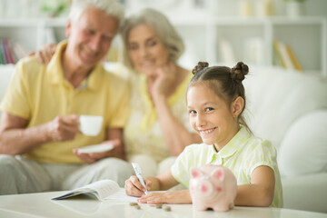 Obraz na płótnie Canvas Portrait of happy grandparents and grandchild with piggy bank at home