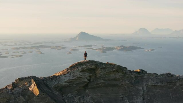 Climber alone on panoramic arctic Norway mountain ridge by ocean; drone orbit