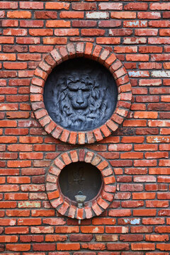 Lion head with mane and bird over fountain on tall red brick wall with circular openings to motifs © Nicholas J. Klein