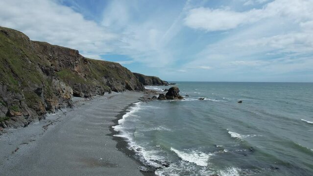 Establishing drone shot moving along the coast and shingle beach at low tide at Tankardstown Beach Copper Coast Waterford Ireland on a blustery summer day
