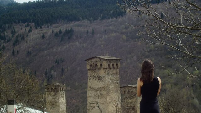 Young woman taking pictures of old stone towers in the mountains. View of traditional ancient Georgian architecture in Svaneti. Cultural heritage