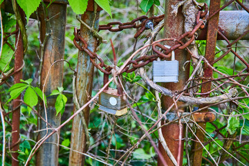 Wrapped rusting chains on rusty iron chain link fence with two corroding padlocks