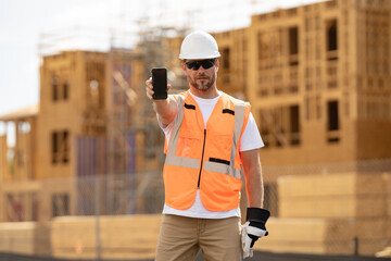 Worker hold phone, builder show phone screen. Architect with mobile phone. Construction site worker in helmet working outdoor. A builder in a safety hard hat at constructing buildings.
