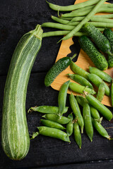 green fresh vegetables on wooden board on black background vertical macro photo
