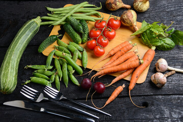 Naklejka na ściany i meble fresh vegetables from the garden on a wooden board on a black background with utensils 