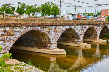 Fototapeta premium Cars crossing over old stone bridge with four arches on underside and flowing river