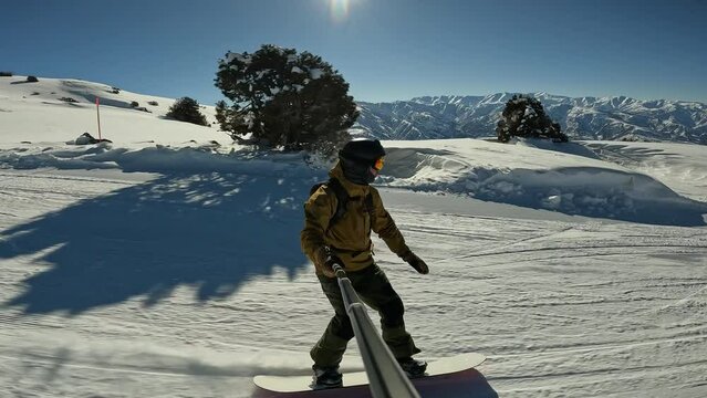 Male millennial cheerful snowboarder having fun snowboarding backcountry on sunny winter day in snowy mountains. Extreme freeride snowboarders riding on snowy track and doing powder turns off piste