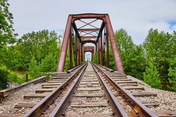 Straight on shot of train tracks leading to rusty old iron railroad bridge with person at end