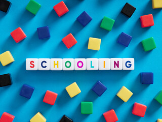 Schooling, education, teaching and learning concept. Colorful cubes on blue background with the word schooling.
