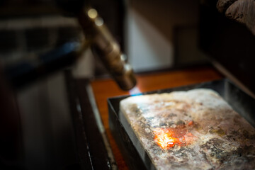 Jeweler melting silver metal with open flame blow torch welding. Goldsmith working and creating in...