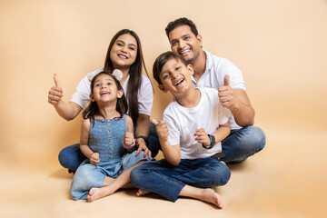 Cheerful young indian parents and kids wearing casual cloths sitting together on floor isolated...