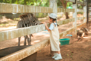 cute baby girl in dress and hat with activity feed food zebra with happy time on outdoor