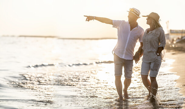 Middle-aged couple on the beach at sunset, the man pointing to a point in the distance. - Powered by Adobe