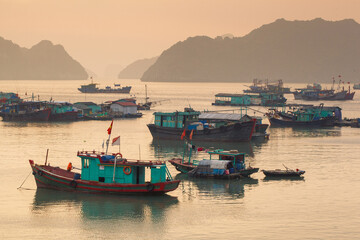 Fototapeta premium Colorful fishing boats on a sea near to rock islands on sunset. Ha Long Bay, Vietnam.