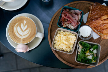Top view of breakfast with eggs,  bacon, salad with pear cheese and arugula, coffee and croissant