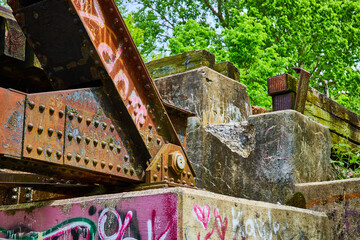Railroad bridge beams with rivets and graffiti on it and concrete wall with damage