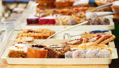 Confectionery stand with a variety of desserts, punch balls coated in grated coconut, brownies sprinkled with almonds and poppy seed swirl in the foreground.