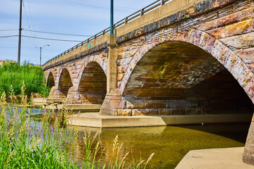 Gorgeous old stone bridge with stone arch underside and river flowing underneath in summer