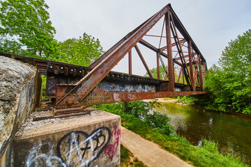 Side view of rusty iron truss train bridge with Heart of Ohio Trail path and Kokosing River