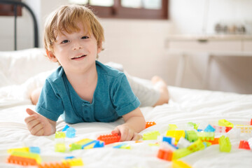 Happiness child playing developing colorful blocks. Smiling Kids play alone with a toy on bed at home. Kindergarten education game. Learn and Play Concept.