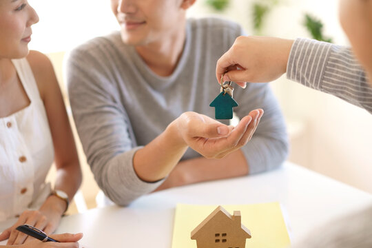 Happy couple receiving keys from new own property, finish meeting in real estate agency lead by realtor. Real estate purchase, success business contract deals with sale represent.