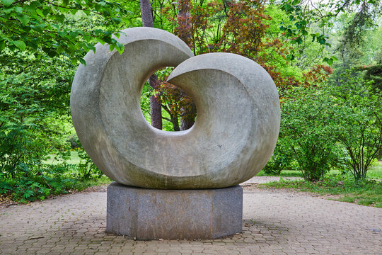 Abstract art stone sculpture of curving rock on cobblestone path with forest nature surrounding
