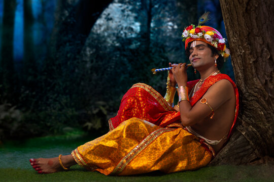 Young man dressed up as Lord Krishna and playing flute on the occasion of Janmashtami