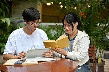 Two smart and focused young Asian college students are sitting at a cafe in an outdoor area