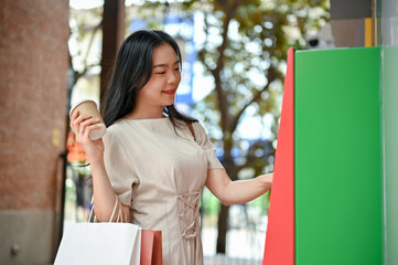 A beautiful Asian woman withdraws her money from an ATM, using an ATM in the city
