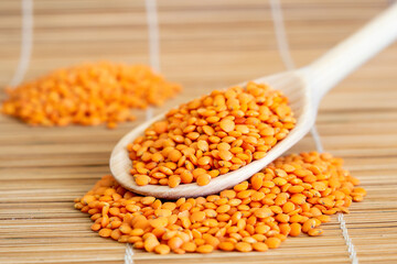 A wooden spoon filled with lentils on top of a bamboo mat