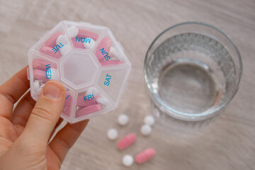 Woman sorting pills Organizer weekly shots Closeup of medical pill box with doses of tablets for daily take medicine with white pink drugs and capsules. Young woman getting her daily vitamins at home